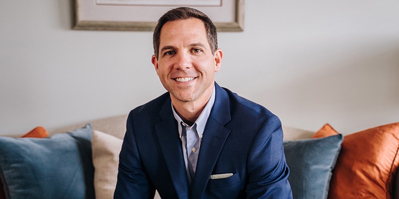 Brad Breeding sitting on a couch in a blue suit smiling